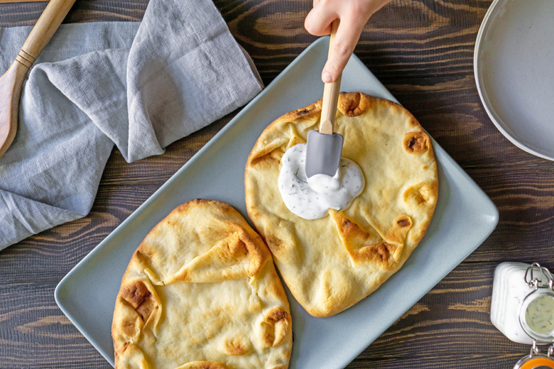 Lemon yogurt dill sauce being spread onto toasted naan