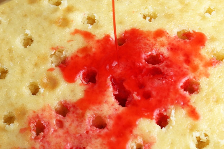 Cherry JELLO Mix pouring into poked cake 