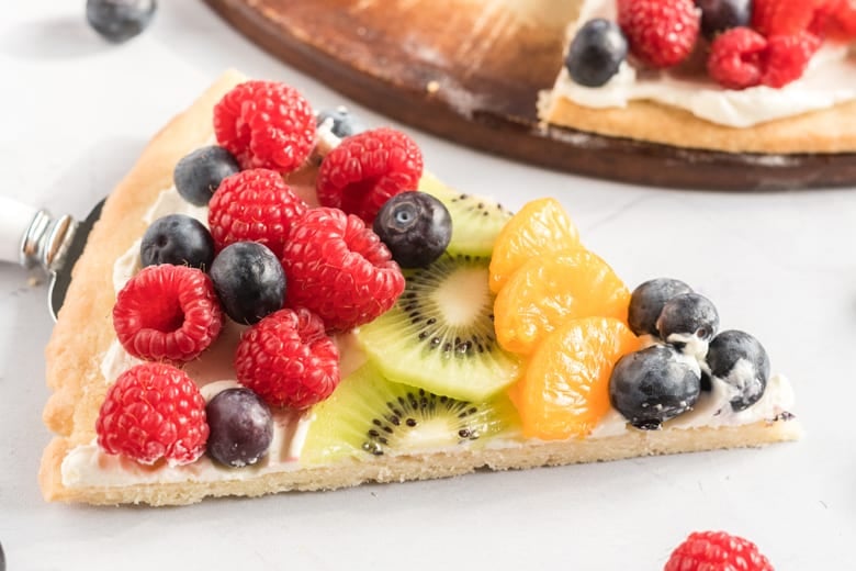 slice of dessert pizza with fresh fruit including raspberries, blueberries, kiwi and oranges 