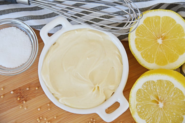 mustard aioli sauce in a white bowl with lemon and a whisk 