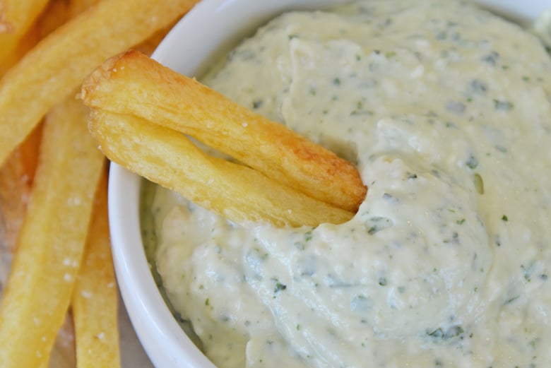 French fries dipping into pesto aioli sauce 
