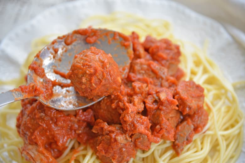 spooning a homemade meatball onto a plate of spaghetti 