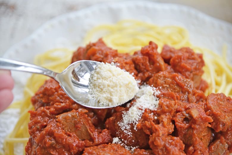 spooning parmesan cheese onto spaghetti sauce 