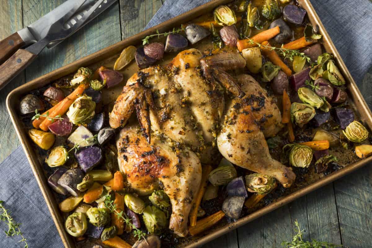 spatchcocked chicken on a baking sheet with roasted vegetables 