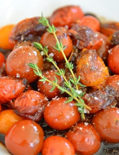 white bowl of stewed tomatoes with thyme garnish