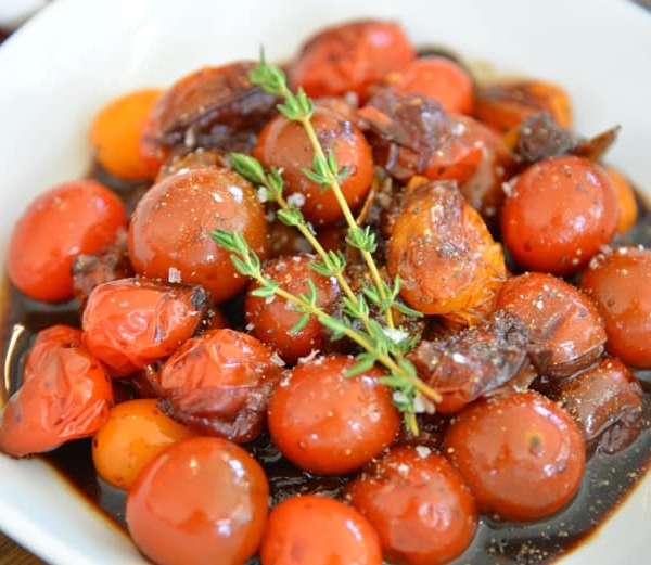 white bowl of stewed tomatoes with thyme garnish