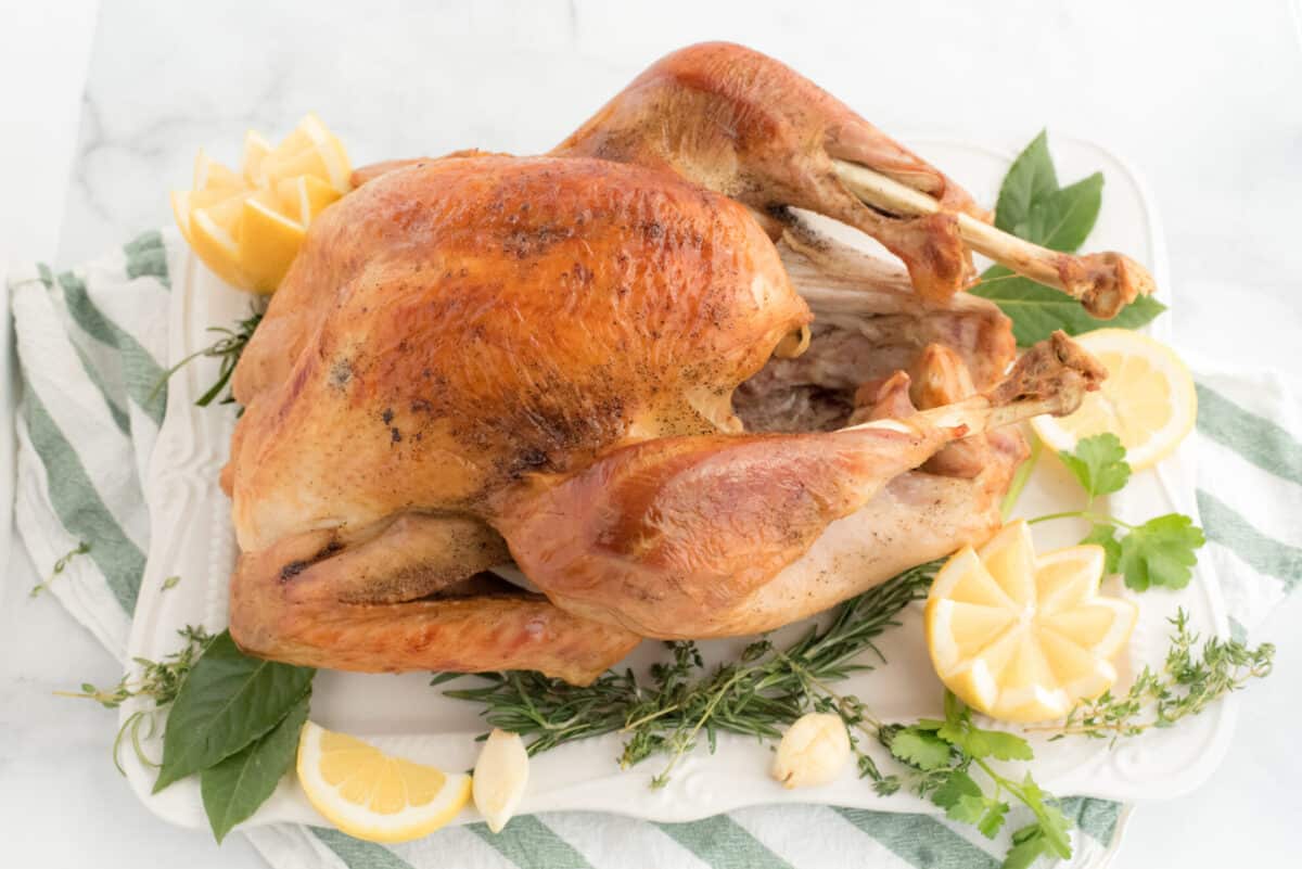 whole turkey on a serving platter with lemons and fresh herbs 