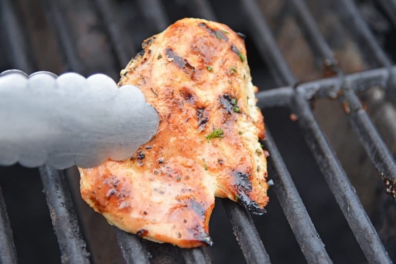 tongs with a piece grilled chicken on the grill 