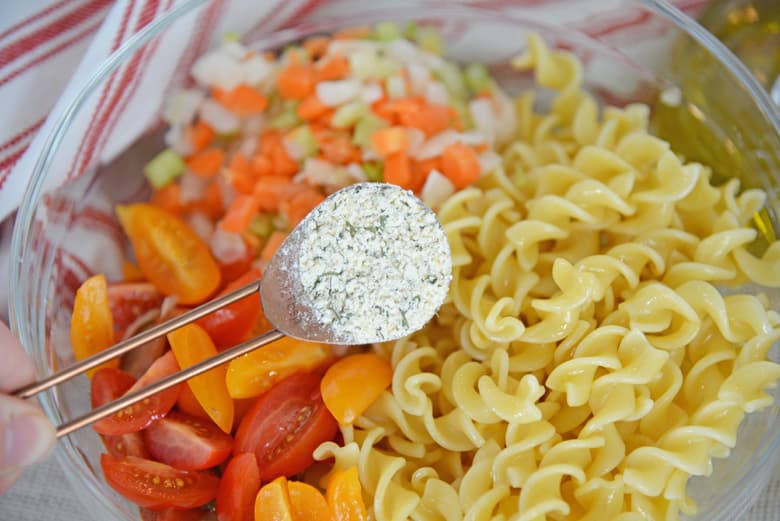 dry ranch seasoning pouring into pasta salad with carrots, celery, onion and tomatoes 