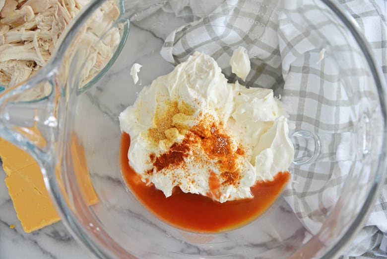 ingredients for buffalo chicken dip in a clear glass mixing bowl 