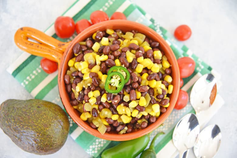 overhead og black bean corn salad in a orange serving bowl with avocado and tomatoes 