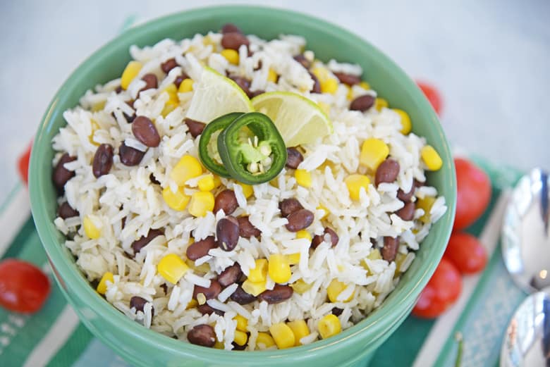 white rice with beans, corn, jalapeno and lime wedges in a green serving bowl 