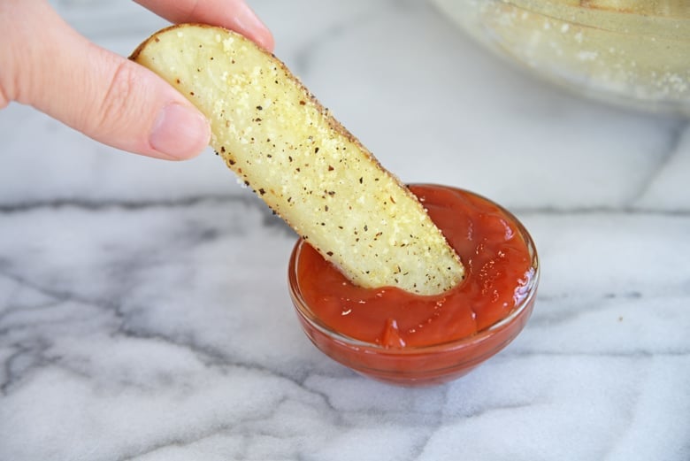 potato wedge dipping into a bowl of ketchup  