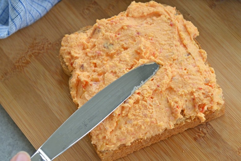 butter knife spreading pimento cheese onto whole wheat bread 