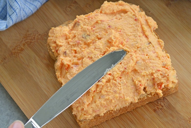 butter knife spreading pimento cheese onto whole wheat bread