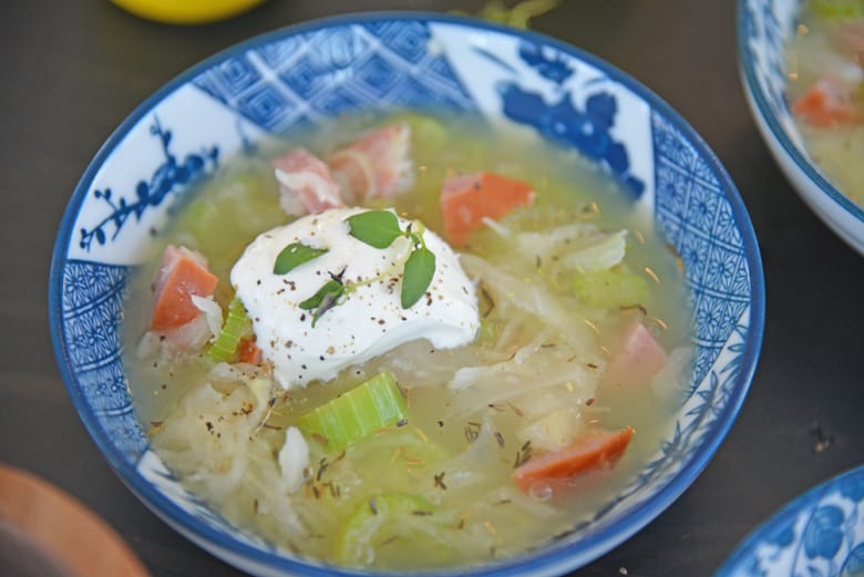 angle view of sauerkraut and kielbasa soup with sour cream and thyme garnish 