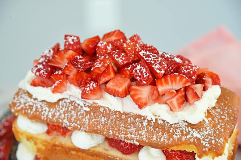 macerated strawberries on top of strawberry shortcake cake with powdered sugar 