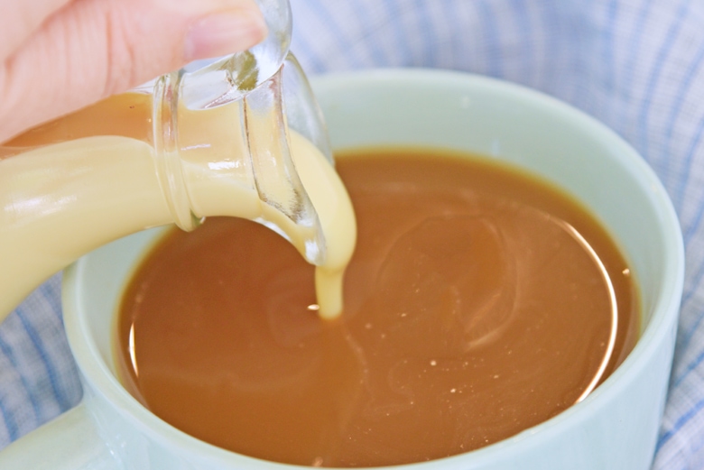 sweetened condensed milk pouring into a cup of coffee 