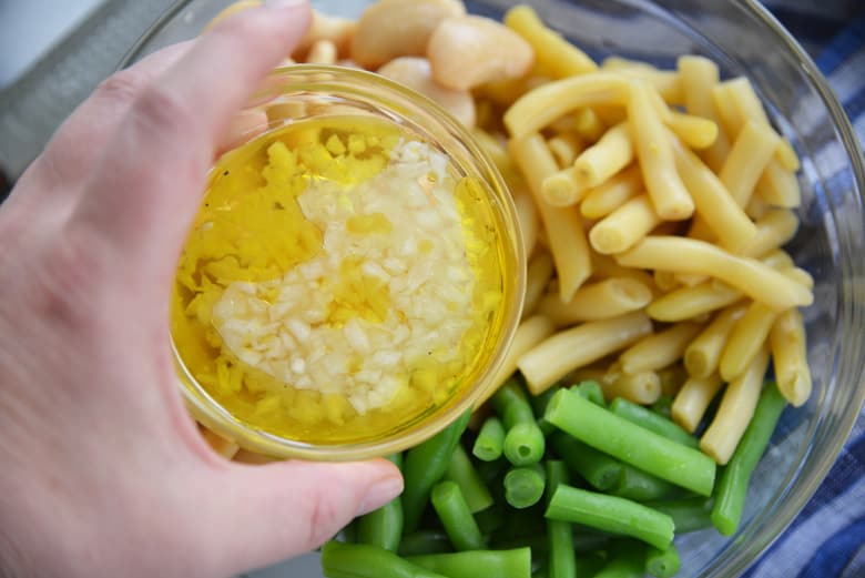 pouring white vinegar dressing over bean salad 