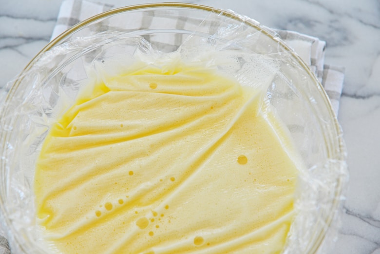 liquid egg custard in a mixing bowl covered with plastic wrap 