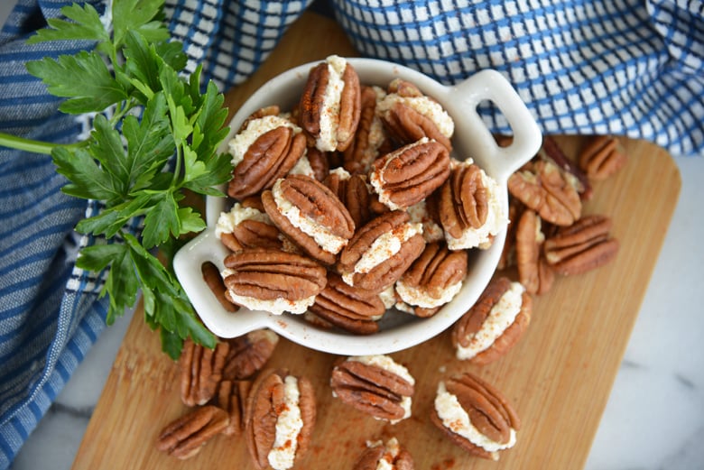 overhead of stuffed pecans in a white serving dish on wood cutting board 