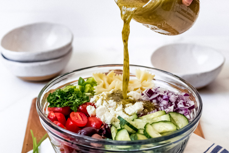 pouring dressing on Greek Pasta Salad 