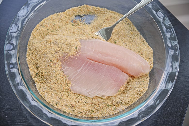 tossing a tilapia fillet in parmesan breading 