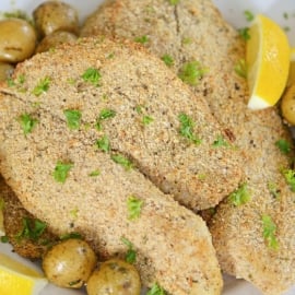 A plate of breaded tilapia with lemons and parsley