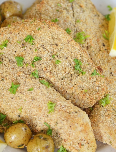 A plate of breaded tilapia with lemons and parsley
