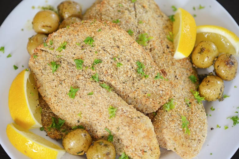 A plate of breaded tilapia with lemons and parsley 