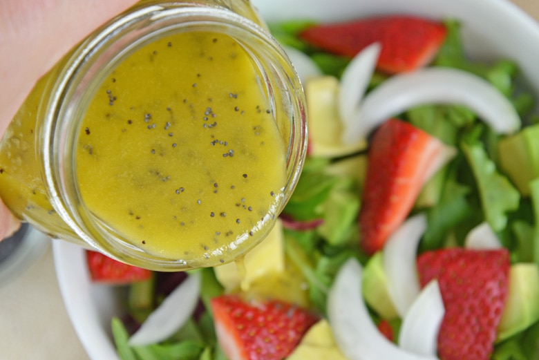 pouring poppy seed dressing on salad 