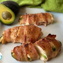 bacon wrapped stuffed chicken on a plate with avocados