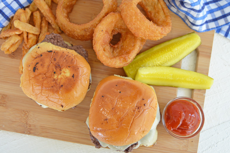 overhead of two smash burgers with onions rings, fries and pickles 