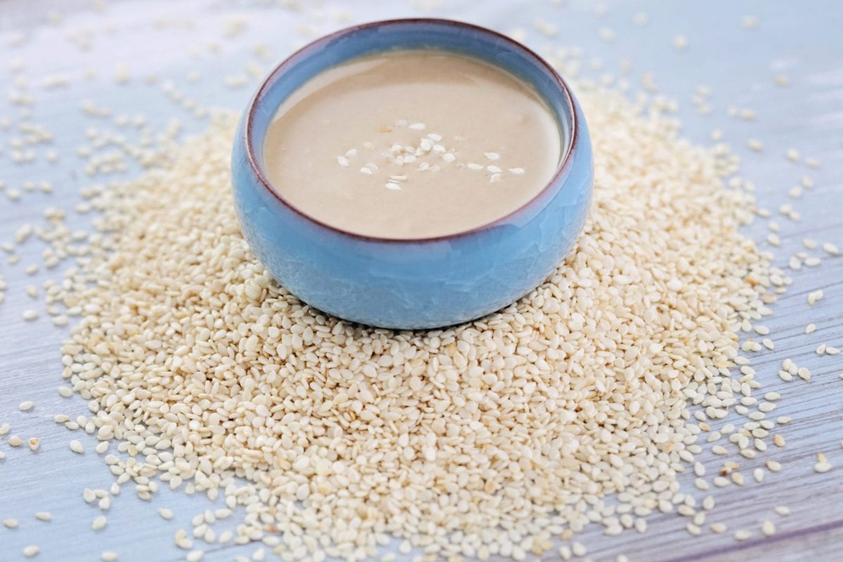 bowl of tahini surrounded by sesame seeds 