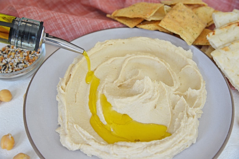 drizzling olive oil onto hummus on a serving plate 