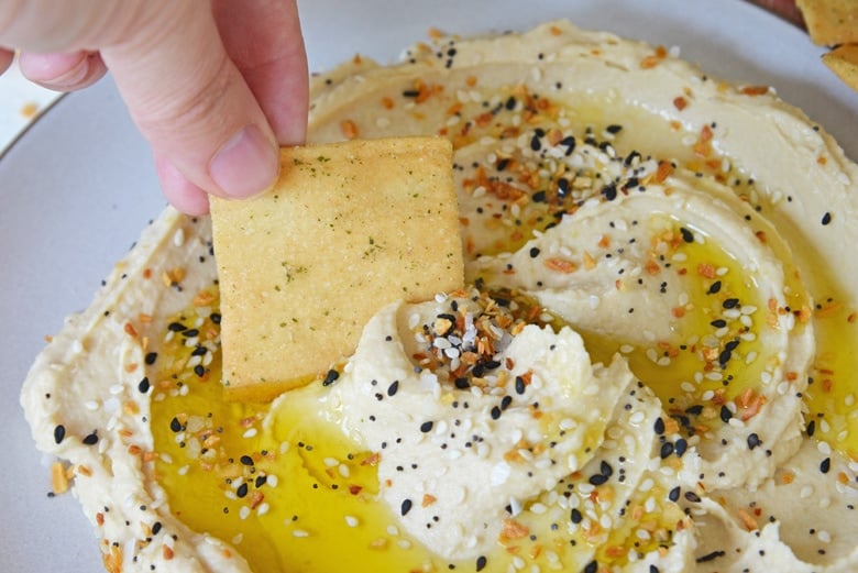 pita chip dipping into hummus with everything seasoning and olive oil 