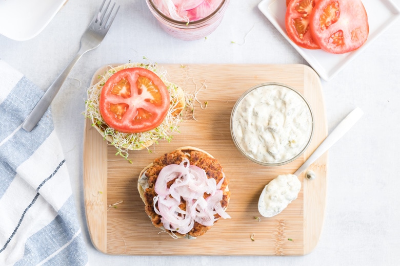 overhead shot of open face salmon burger on wooden board with sauce