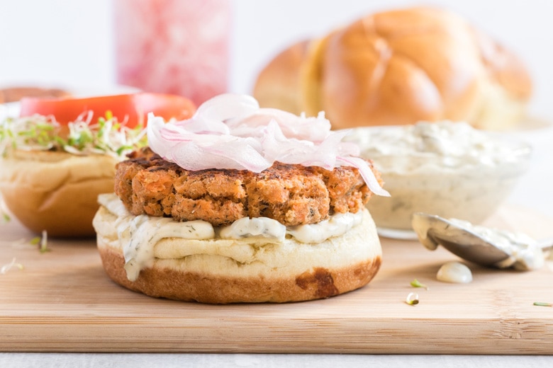 straight on shot of open face salmon burger on wooden board