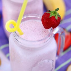 strawberry banana smoothie in mug with straw and strawberry in it