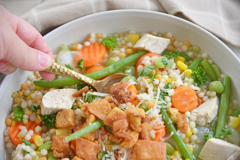 gold spoon dipping into bowl of turkey noodle soup  