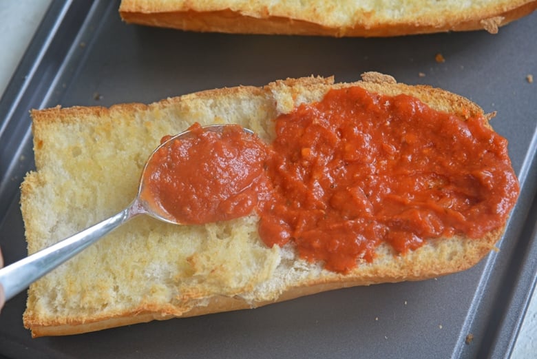 spooning tomato sauce onto a slice of french bread 