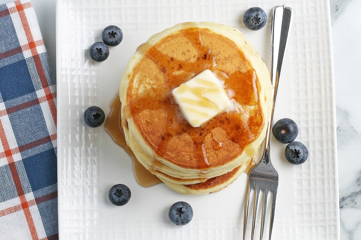 overhead of a stack of pancakes with fruit, butter and syrup 