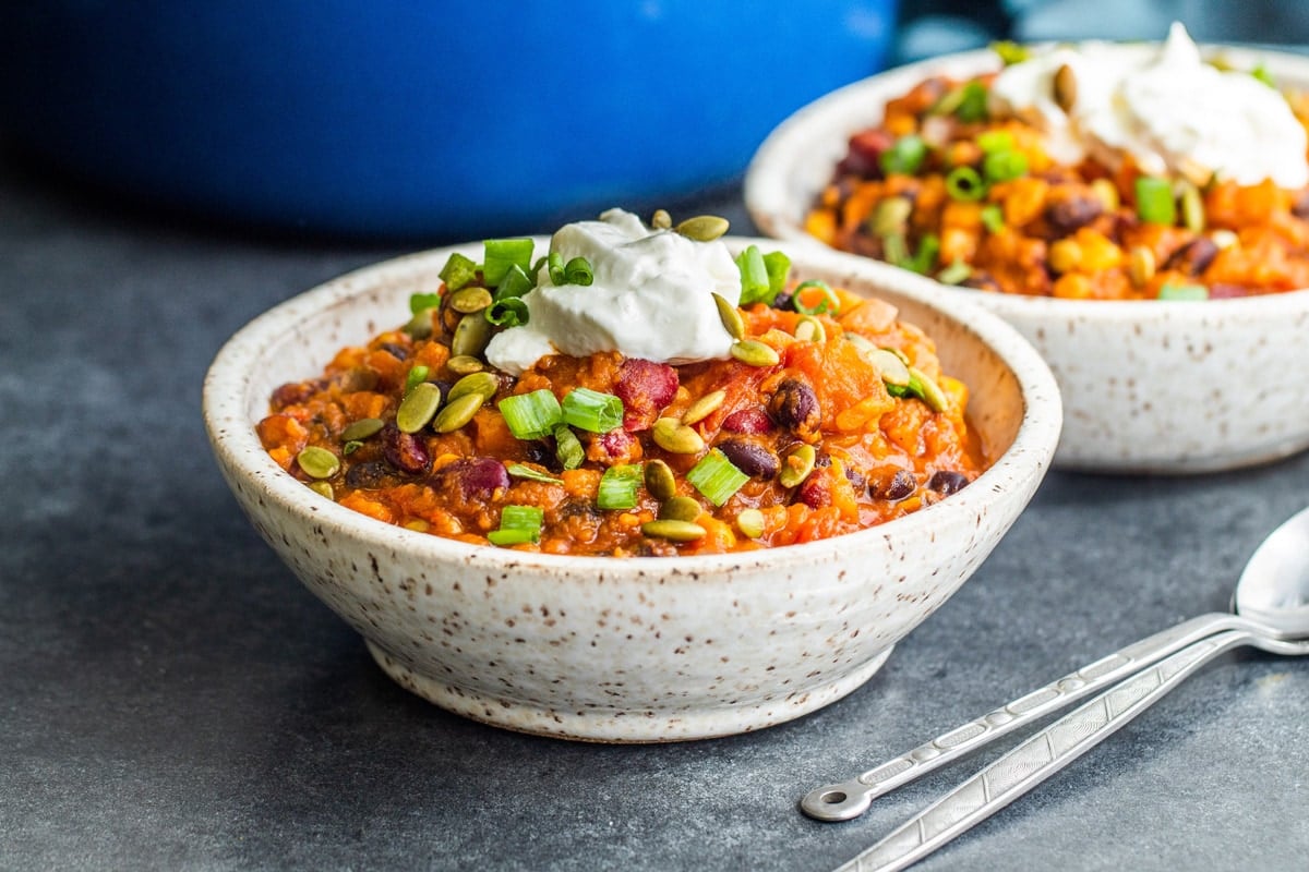 two bowls sweet potato chili on a table with spoons 