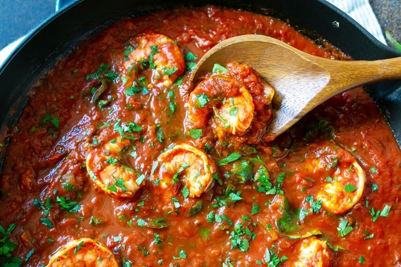 wooden spoon with shrimp and fresh herbs in a tomato sauce 