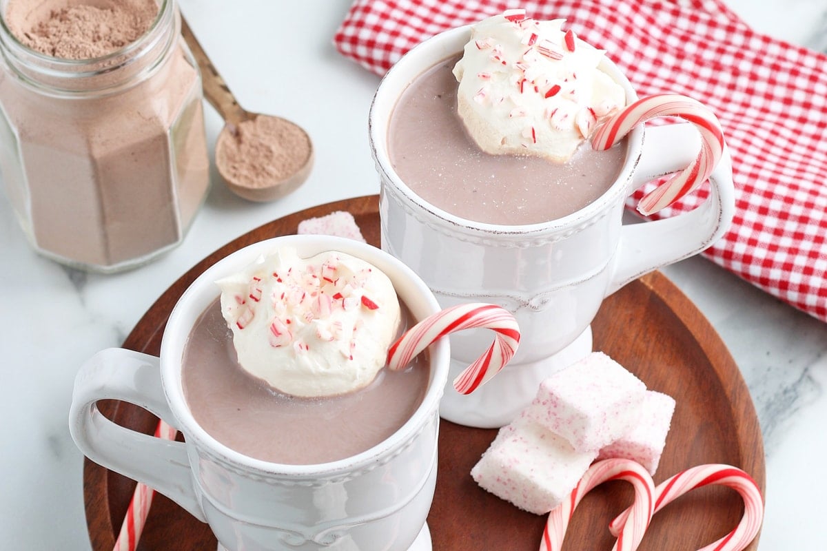 overhead of two mugs of hot chocolate topped with whipped cream and peppermint 
