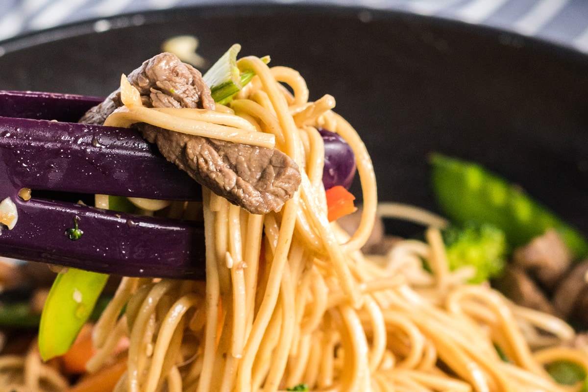 tongs holding up beef lo mein 