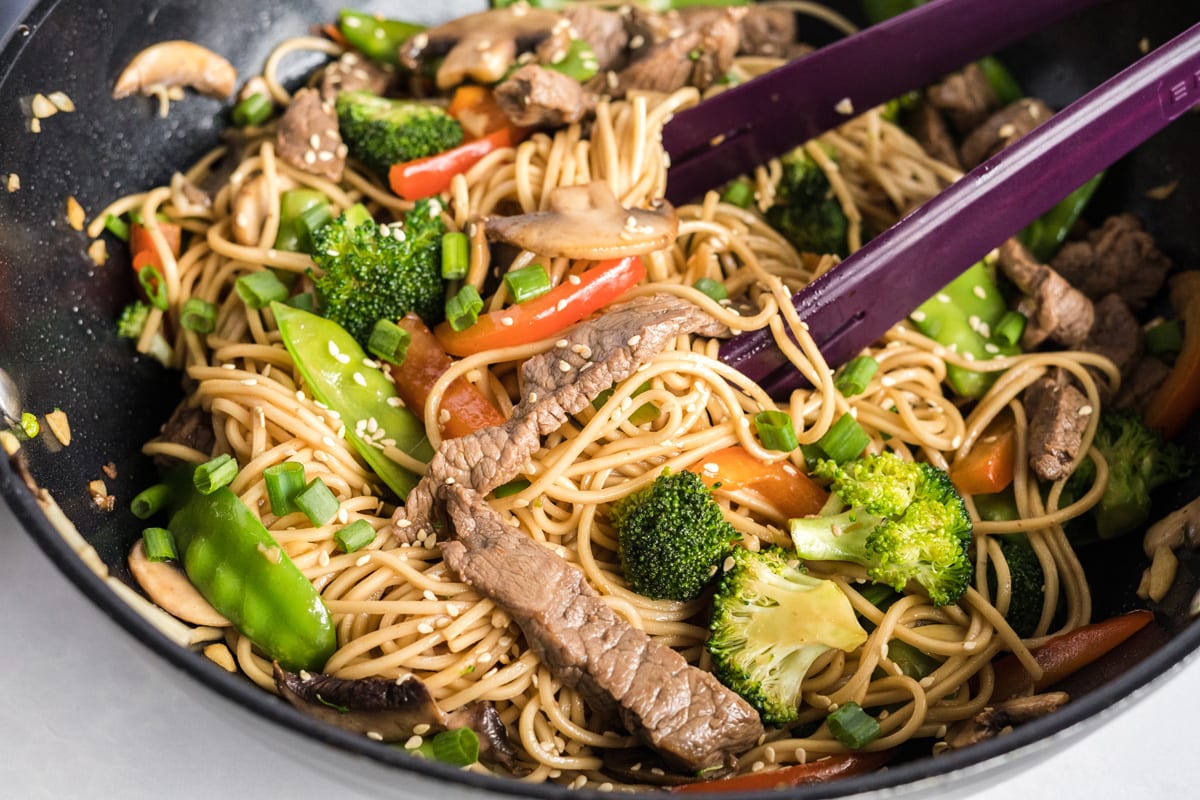 tongs in a skillet of beef lo mein 