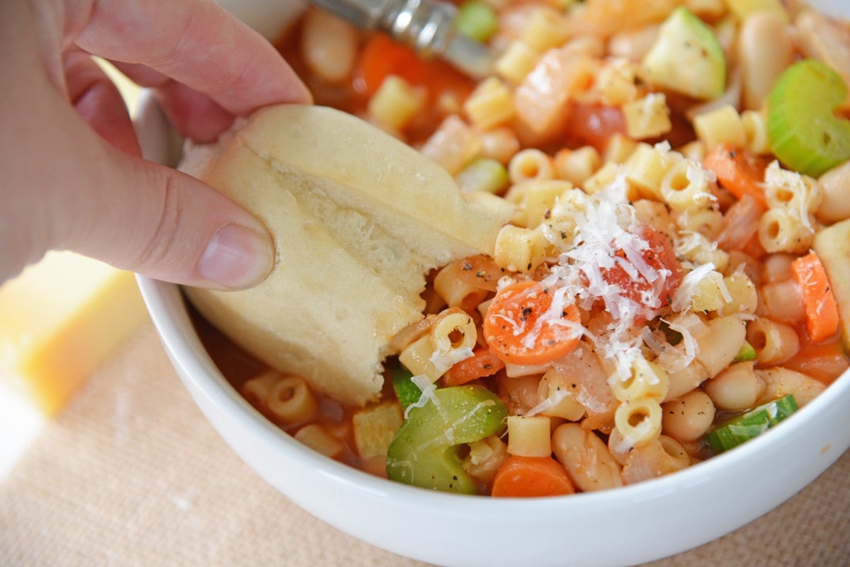 roll dipping into minestrone soup 