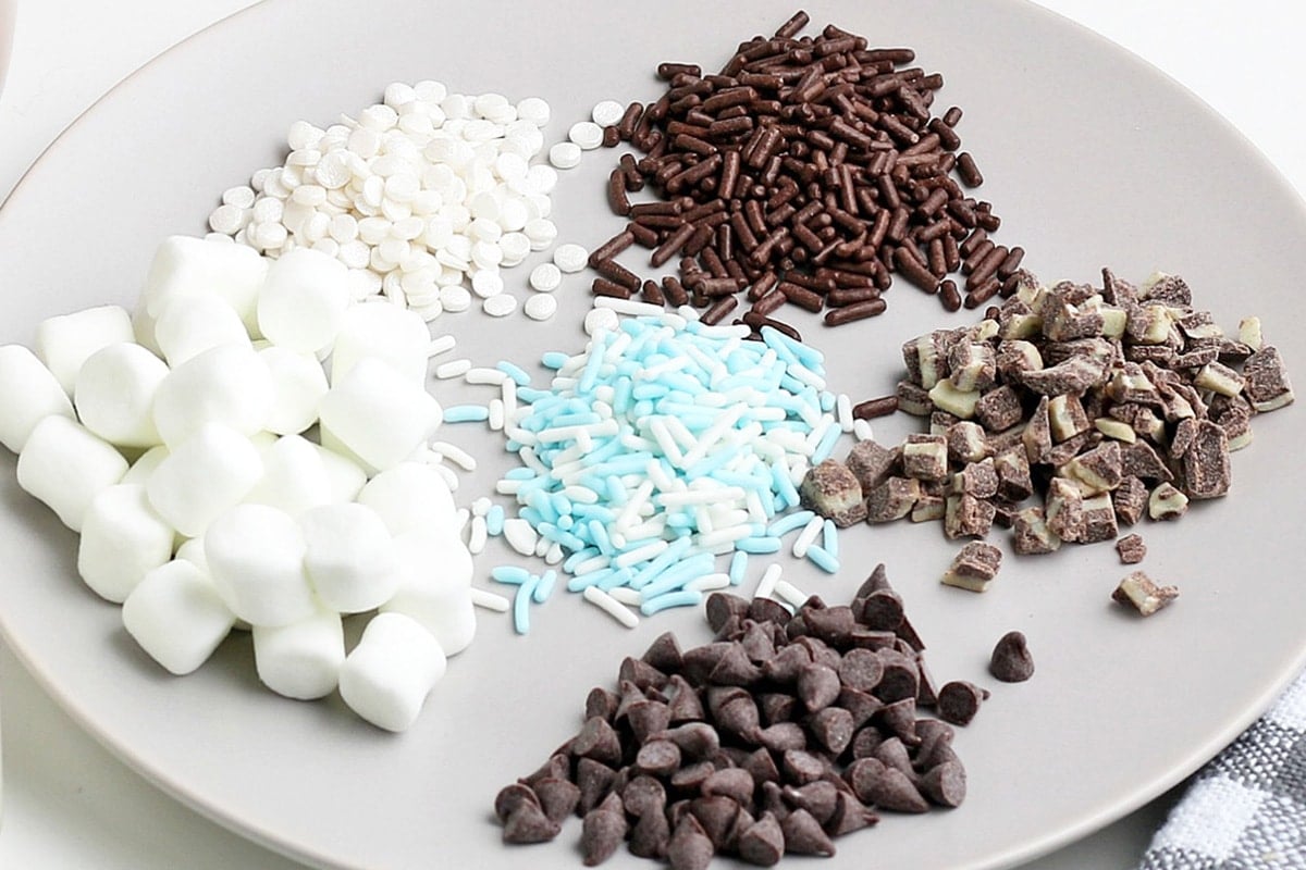 angled shot of plate of toppings like sprinkles, marshmallows and chocolate chips