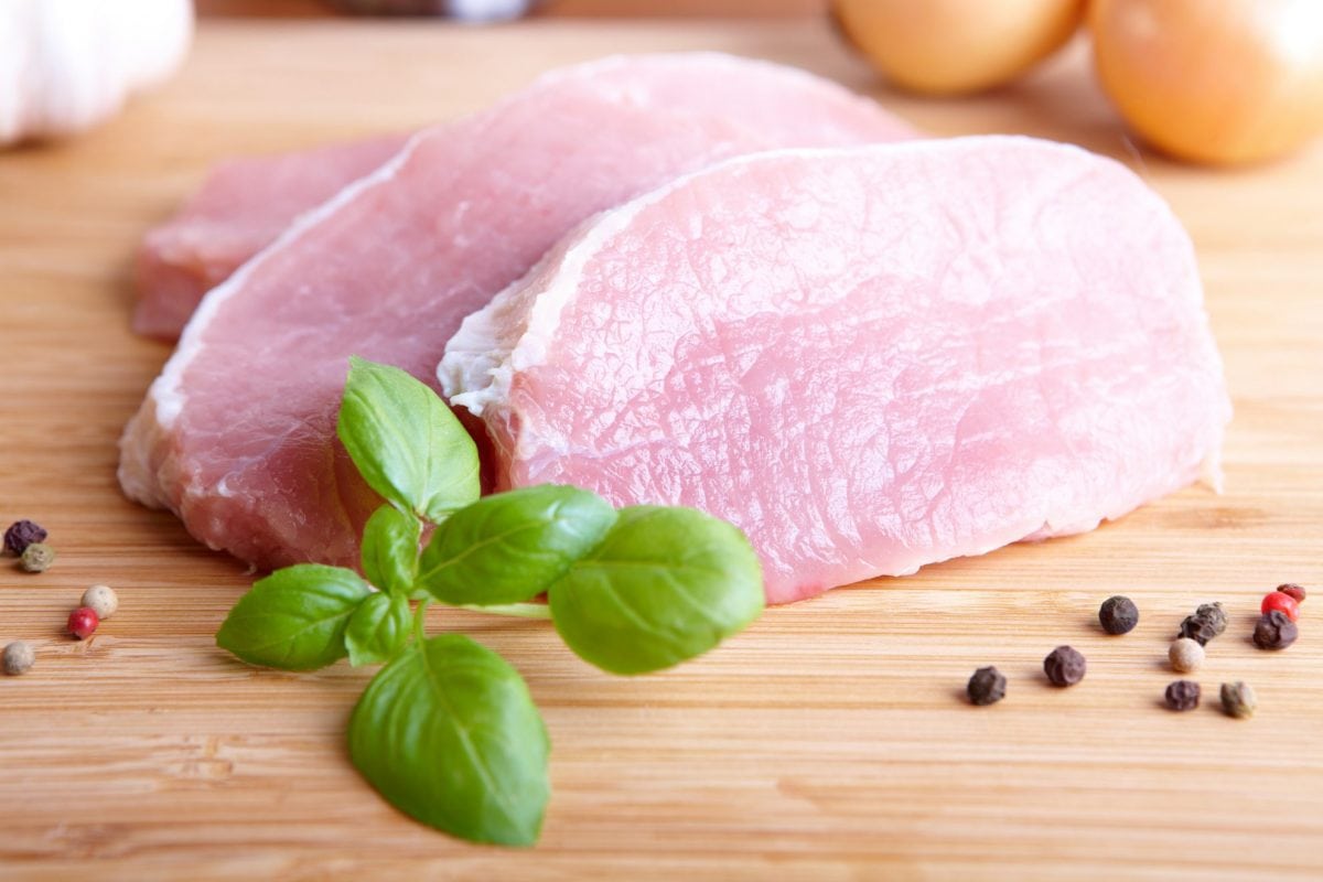 raw pork chop on a cutting board with basil 